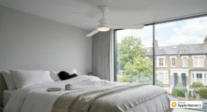 A white HomeKit-compatible ceiling fan operating silently in a minimalist UK master bedroom with crisp white linens and soft morning light.