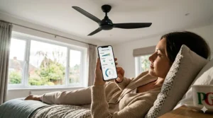 A person using a smartphone app to adjust the speed and timer settings of a smart ceiling fan in a UK bedroom.