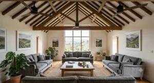 A wide-angle interior view of a bright and inviting British loft conversion master bedroom, featuring a grey fabric headboard, neutral tones, and a sleek white ceiling fan mounted directly onto the sloping whitewashed beam ceiling.