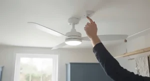 A close-up view of a hand cleaning dust from the blades of a utility room ceiling fan with a cloth.