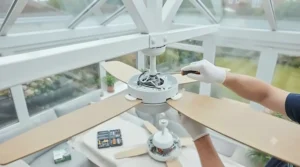 A professional electrician installing an energy-efficient conservatory fan in a vaulted glass roof.