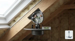 An internal view of a secure, heavy-duty metal junction box correctly mounted to a structural timber rafter within a 45-degree insulated loft space. Electrical wires are neatly connected inside, and the box is positioned to receive the angled fan adapter.