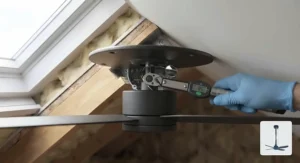 A gloved hand using a calibrated digital torque wrench to perform a final safety check on the fixing bolts of the ceiling fan installed on the 45-degree sloped ceiling. The digital display confirms the correct tightening force.